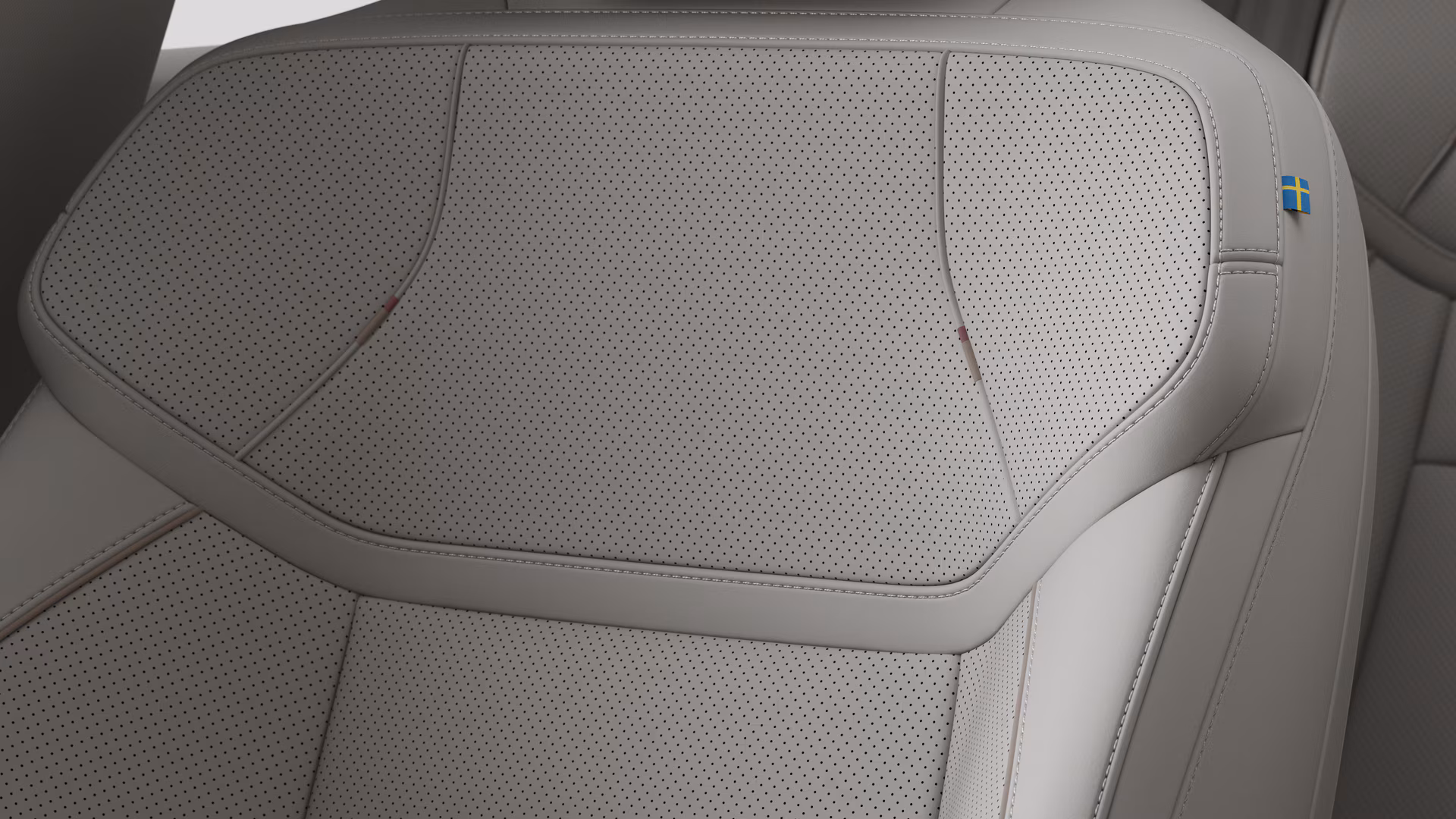 Крупный план деталей салона автомобиля Volvo, на котором видны швы и маленькая бирка с шведским флагом.