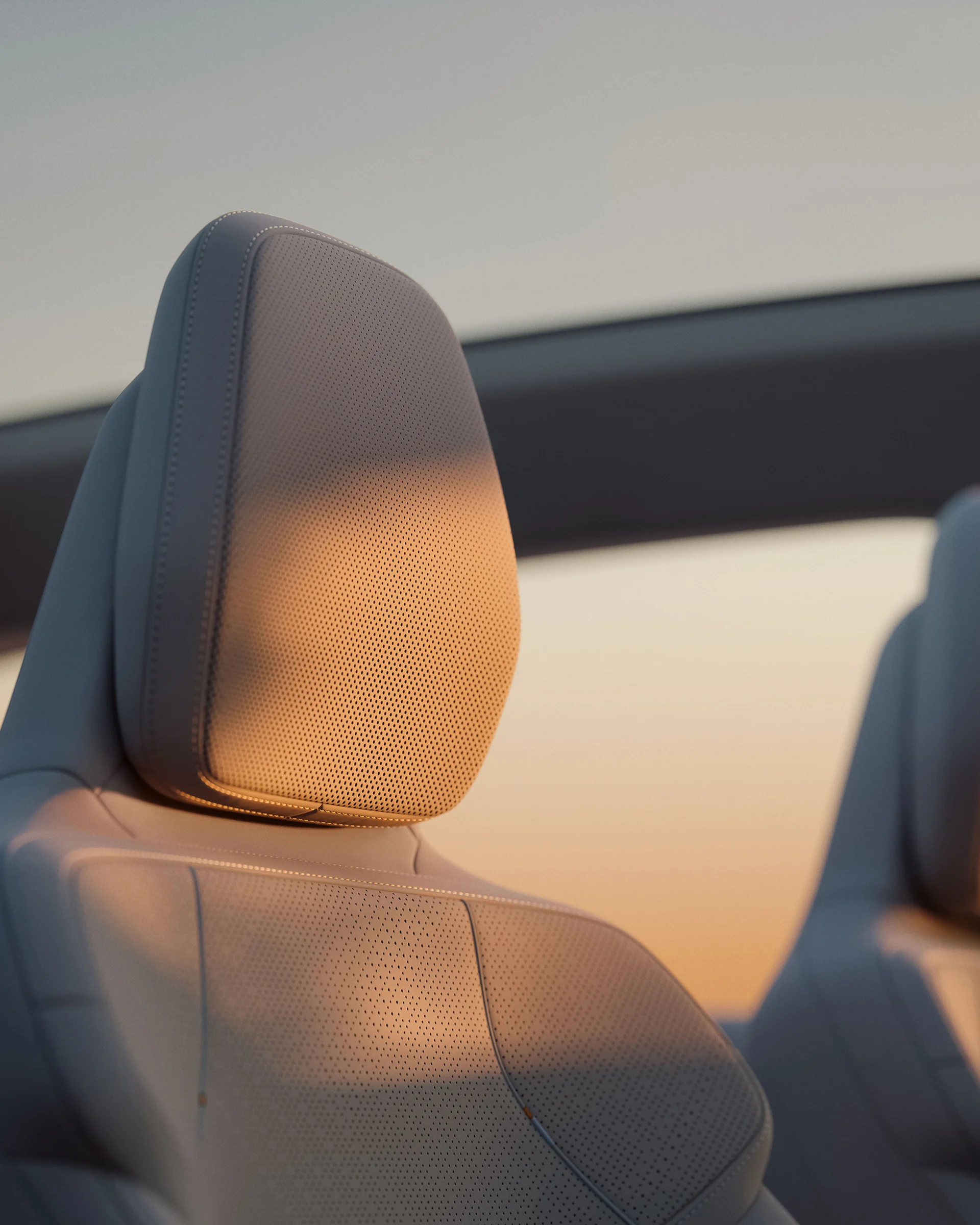 Крупный план подголовника переднего сиденья в Volvo EX60 с мягким освещением на закате. 