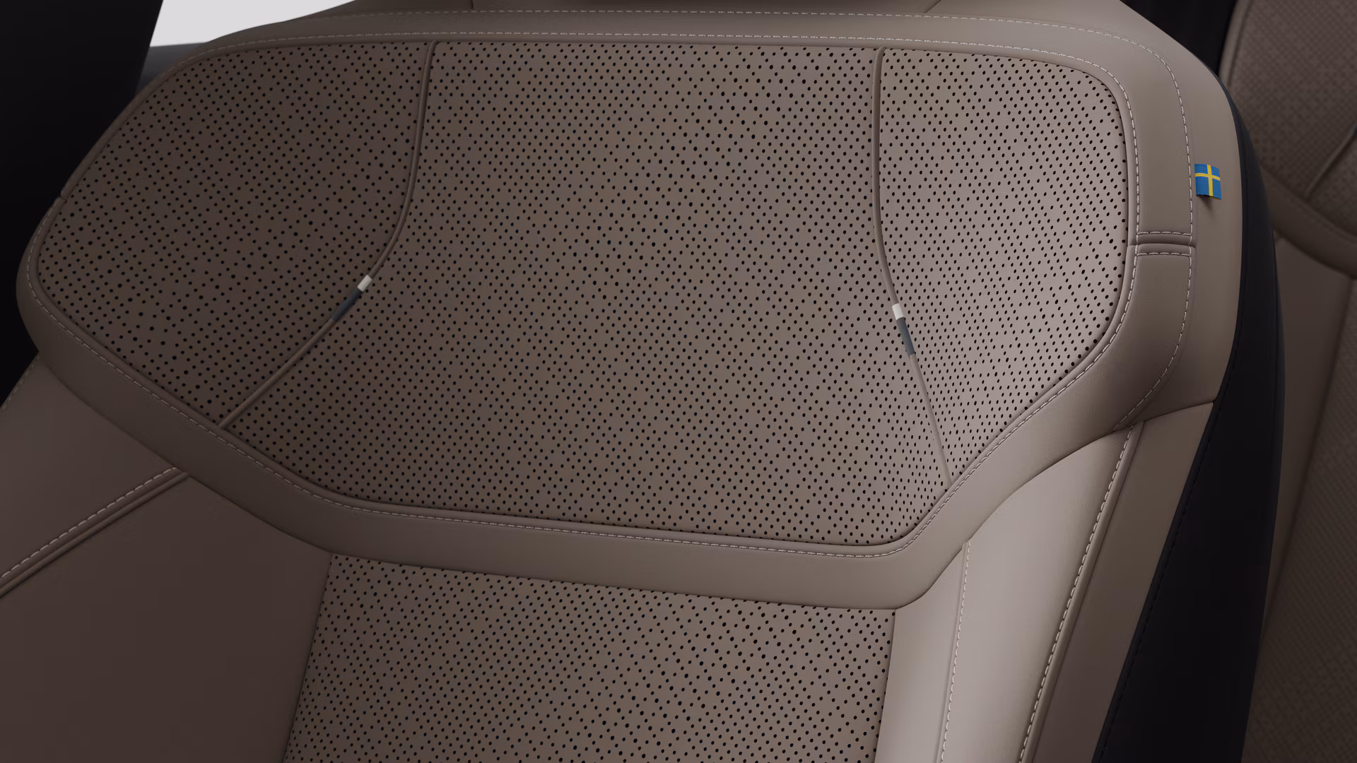Крупный план деталей салона автомобиля Volvo, на котором видны швы и маленькая бирка с шведским флагом.