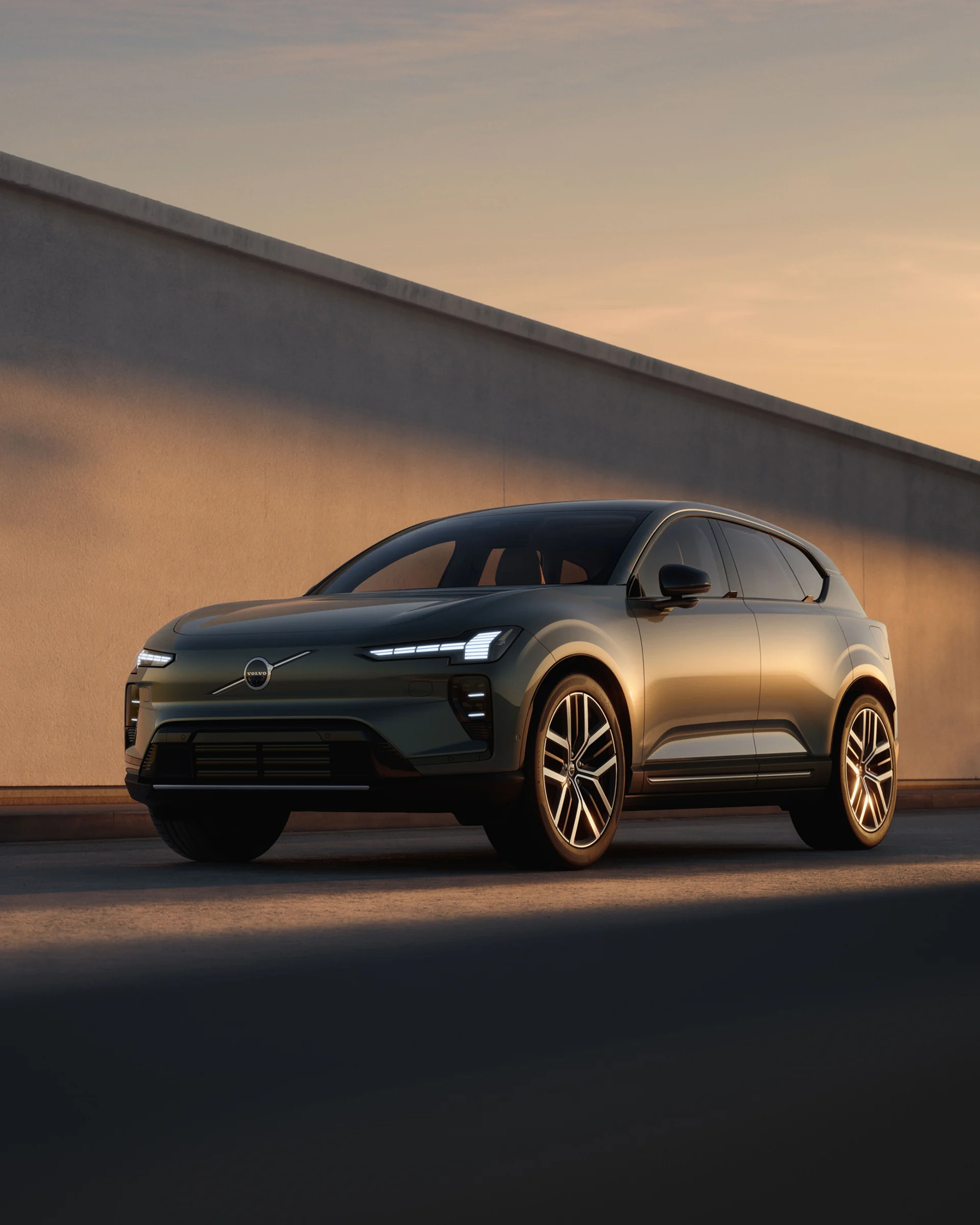 Volvo EX60 припаркован у стены, вид спереди под углом в три четверти при мягком солнечном свете.