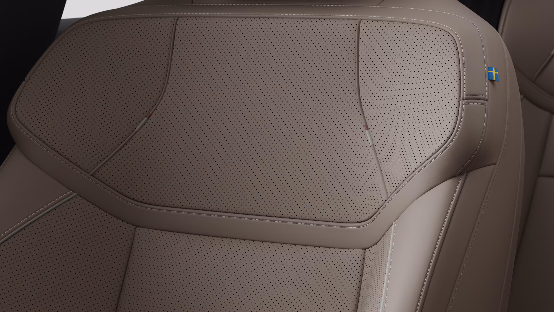Крупный план деталей салона автомобиля Volvo, на котором видны швы и маленькая бирка с шведским флагом.