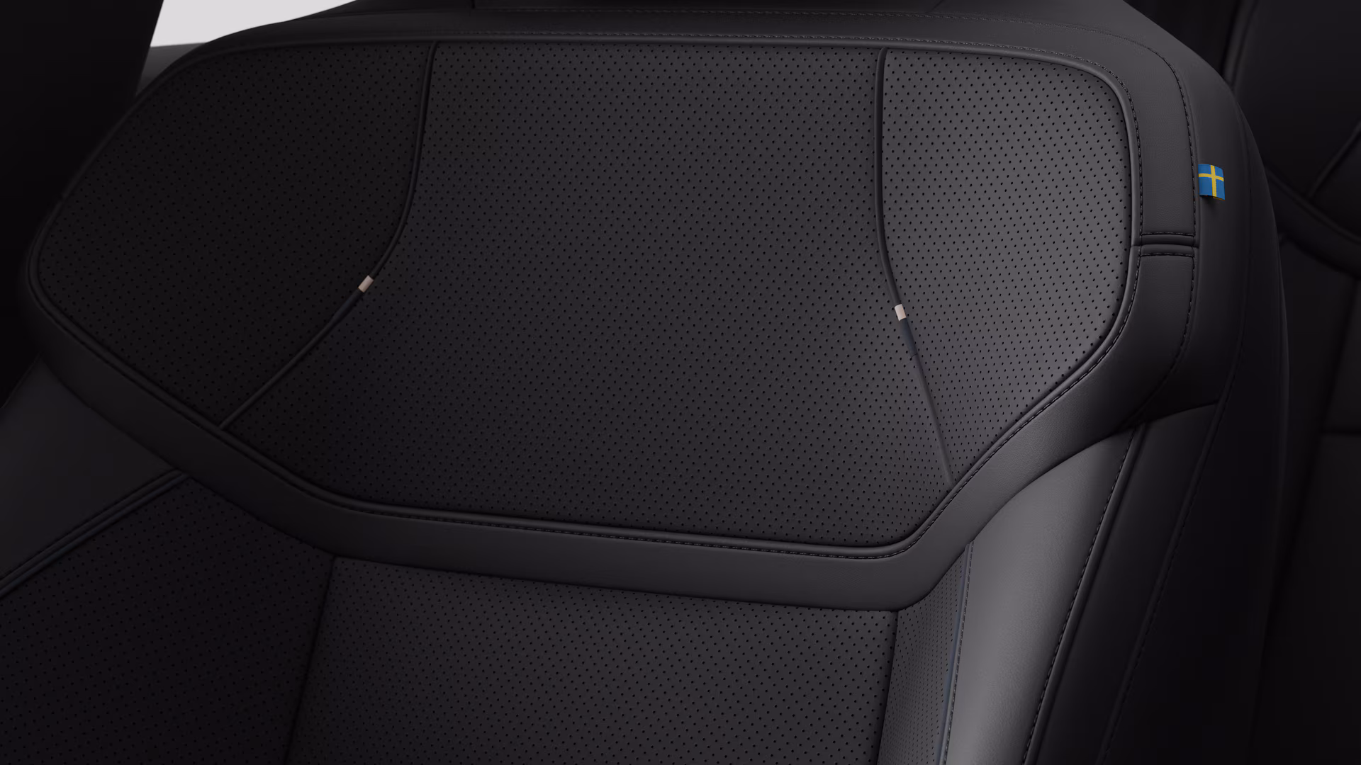 Крупный план деталей салона автомобиля Volvo, на котором видны швы и маленькая бирка с шведским флагом.
