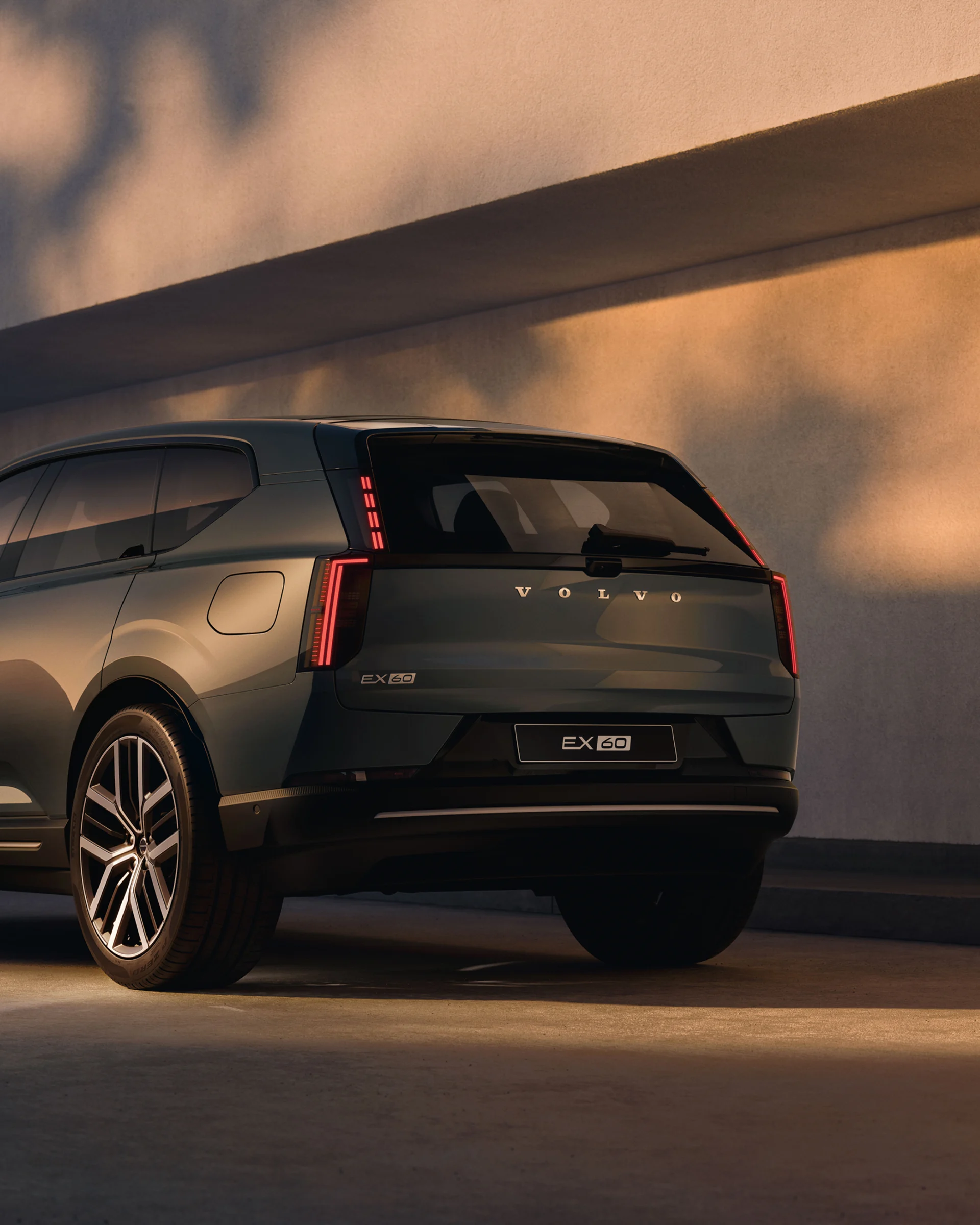 Вид сзади на Volvo EX60, припаркованный перед стеной.