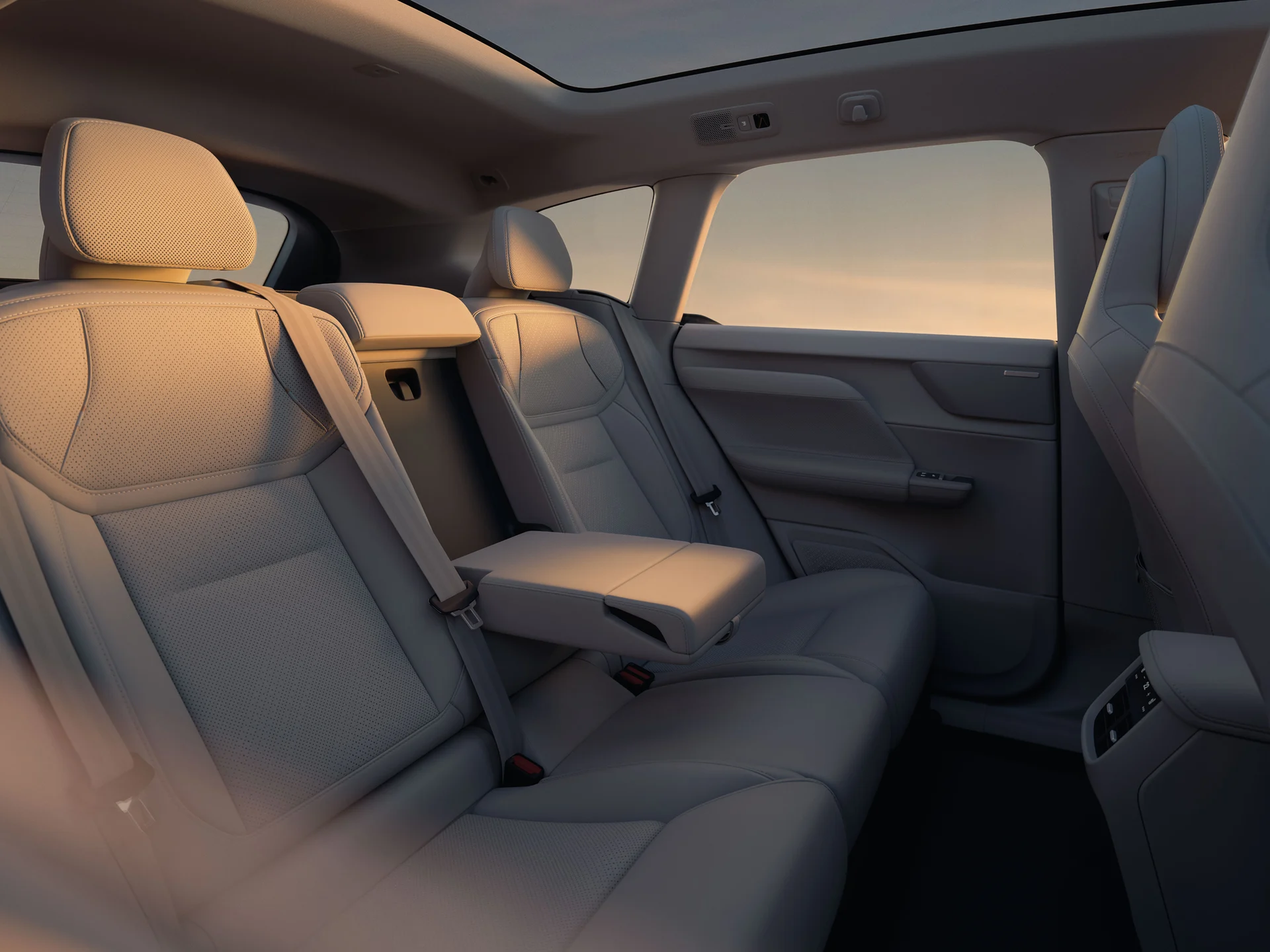 Задние сиденья Volvo EX60 со сложенным центральным подлокотником в теплом вечернем свете.
