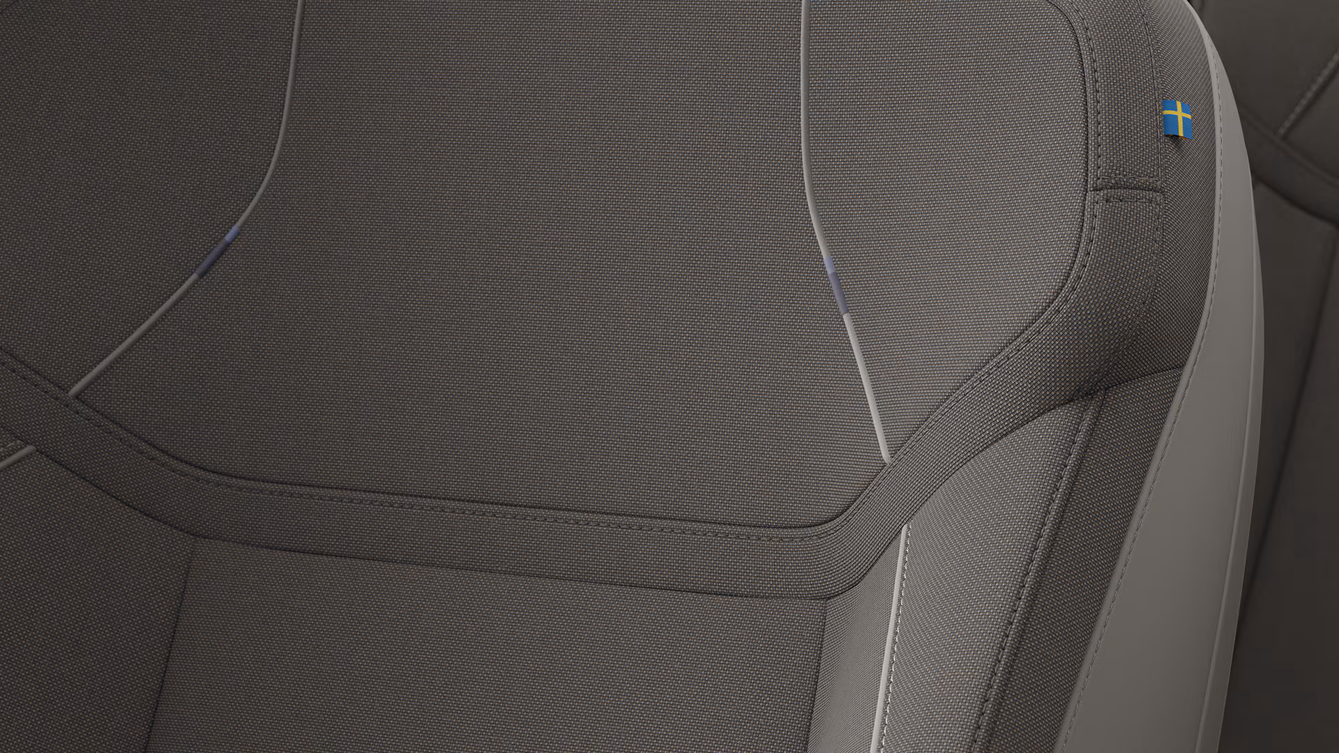 Крупный план автомобильного сиденья Volvo с темной тканевой обивкой и небольшой биркой со шведским флагом в верхнем углу.