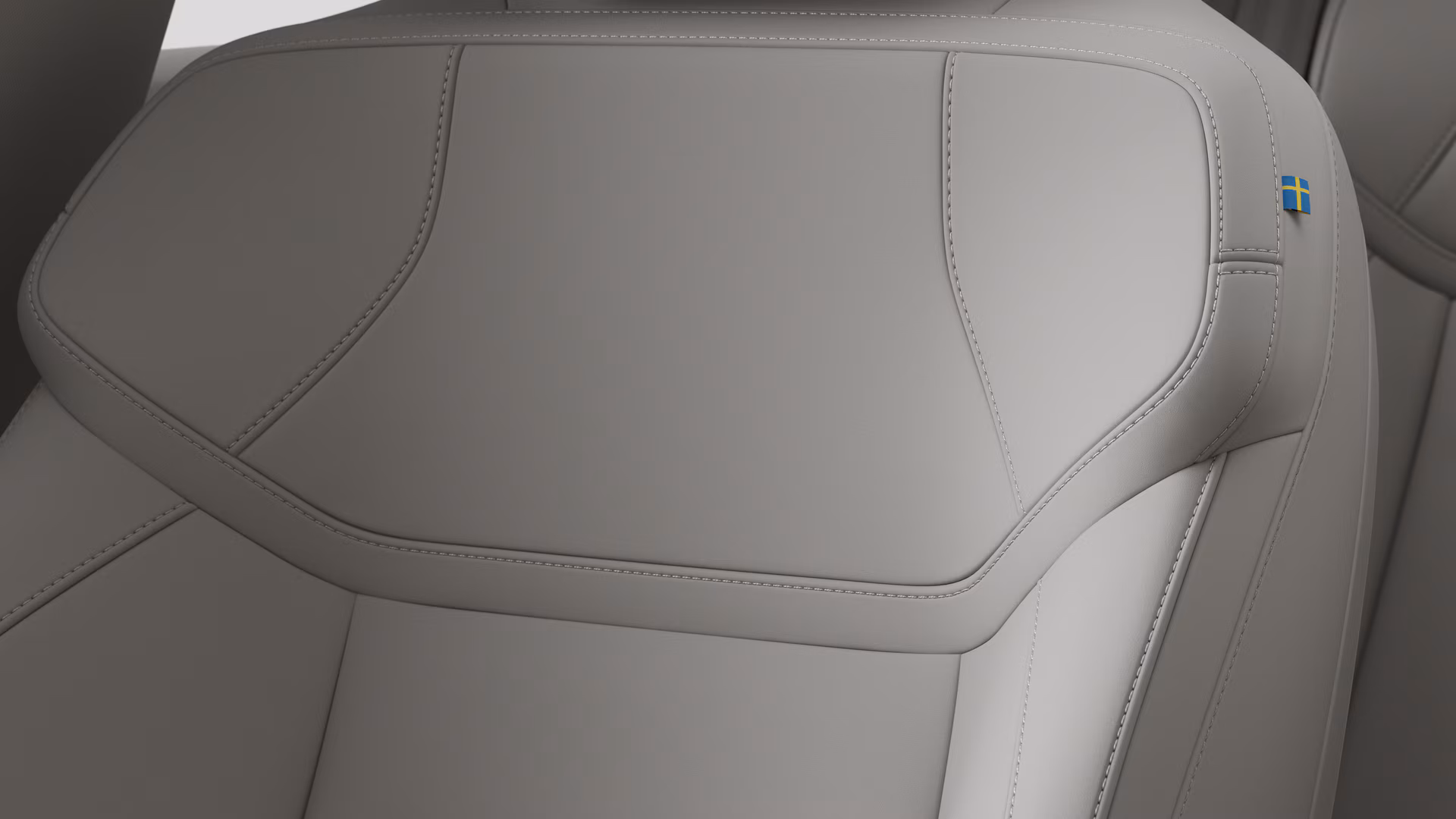 Крупный план деталей салона автомобиля Volvo, на котором видны швы и маленькая бирка с шведским флагом.