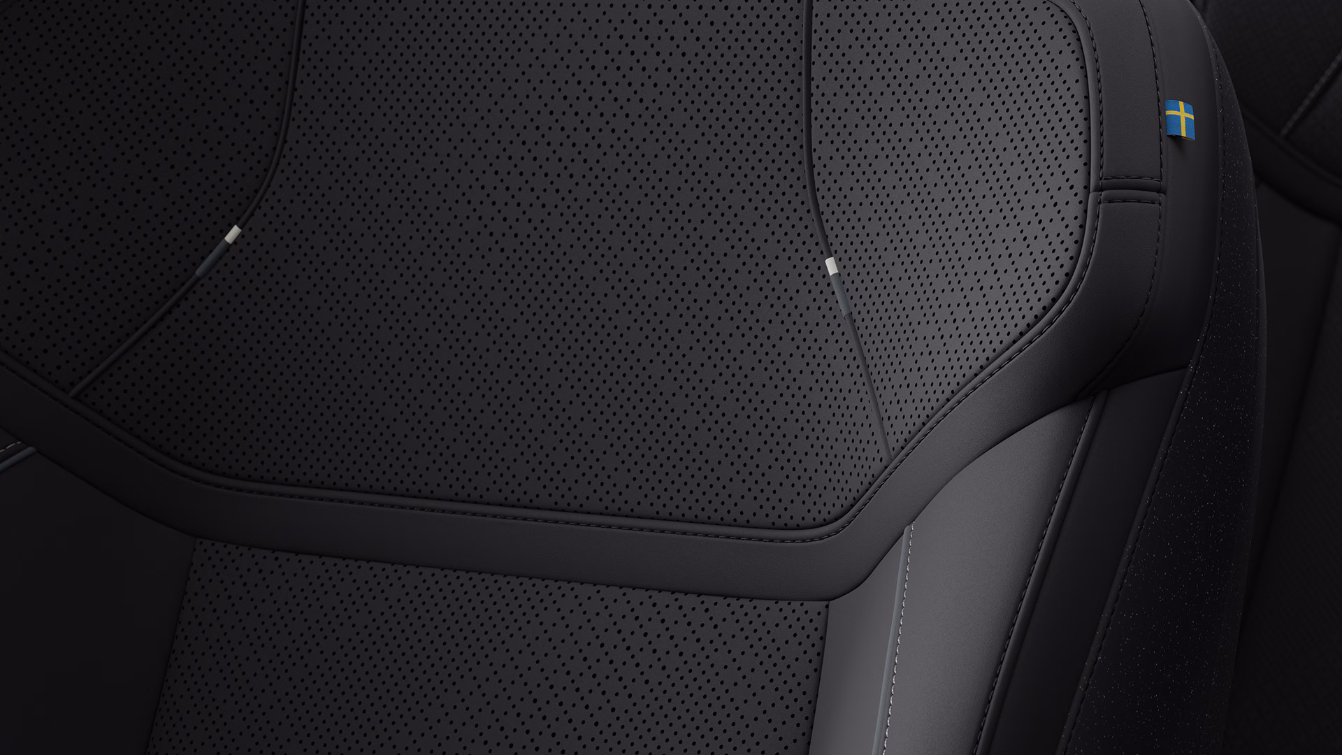 Крупный план автомобильного сиденья Volvo с перфорированной черной обивкой и маленькой биркой со шведским флагом.