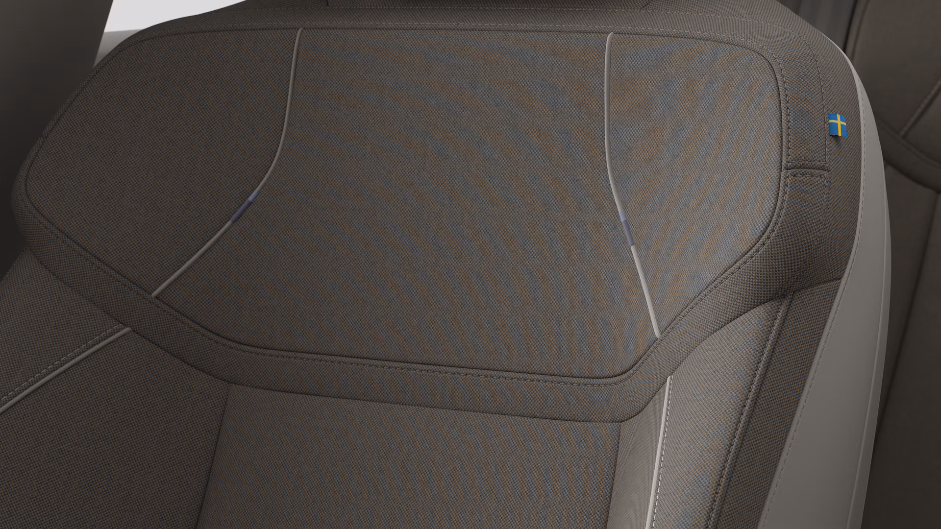 Крупный план деталей салона автомобиля Volvo, на котором видны швы и маленькая бирка с шведским флагом.
