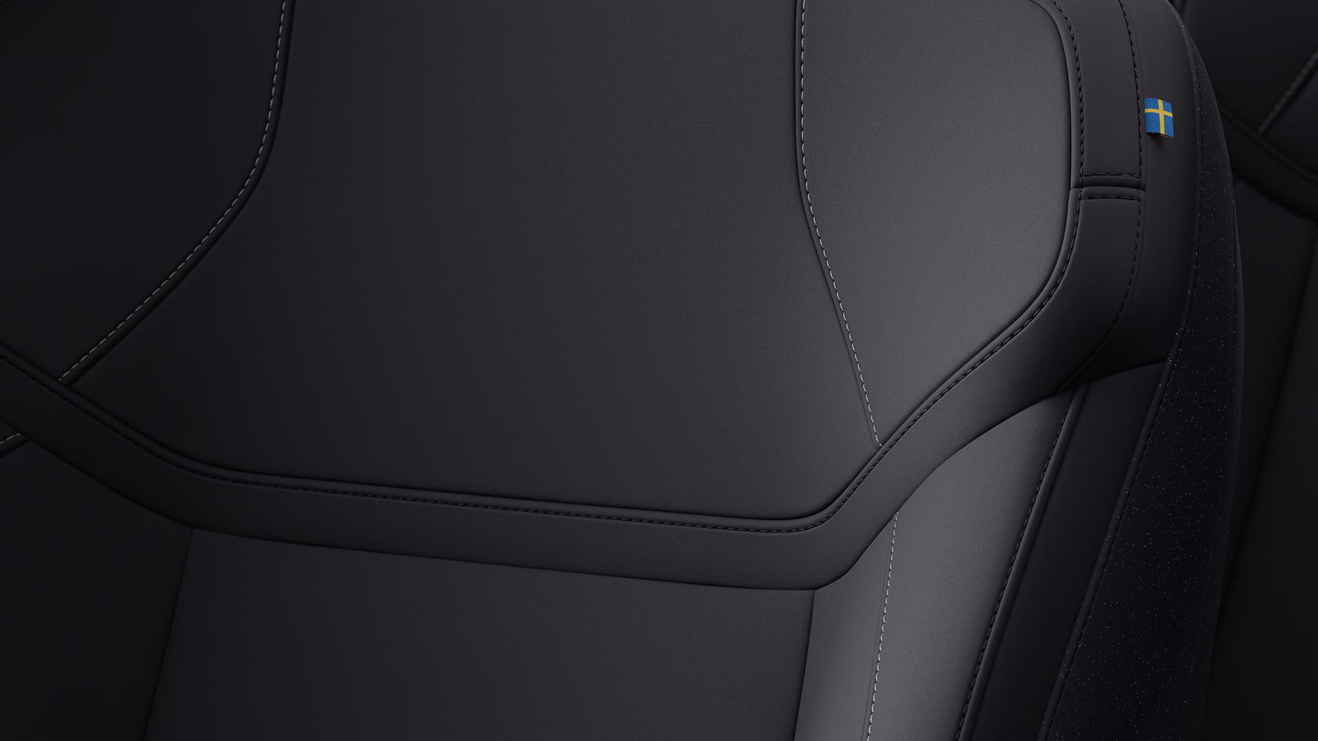 Крупный план автомобильного сиденья Volvo с детальной строчкой и небольшой биркой со шведским флагом в правом верхнем углу.