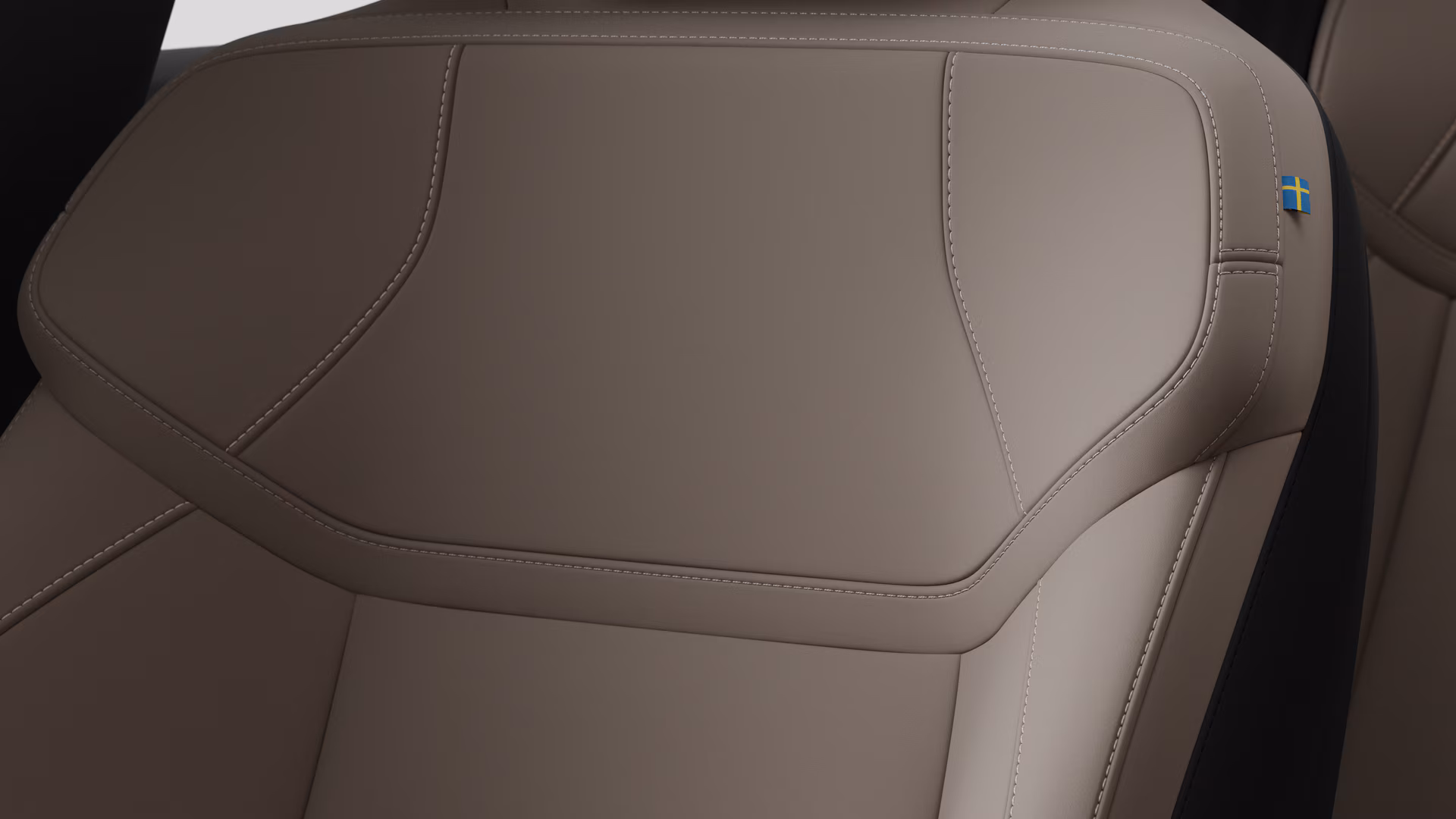 Крупный план деталей салона автомобиля Volvo, на котором видны швы и маленькая бирка с шведским флагом.