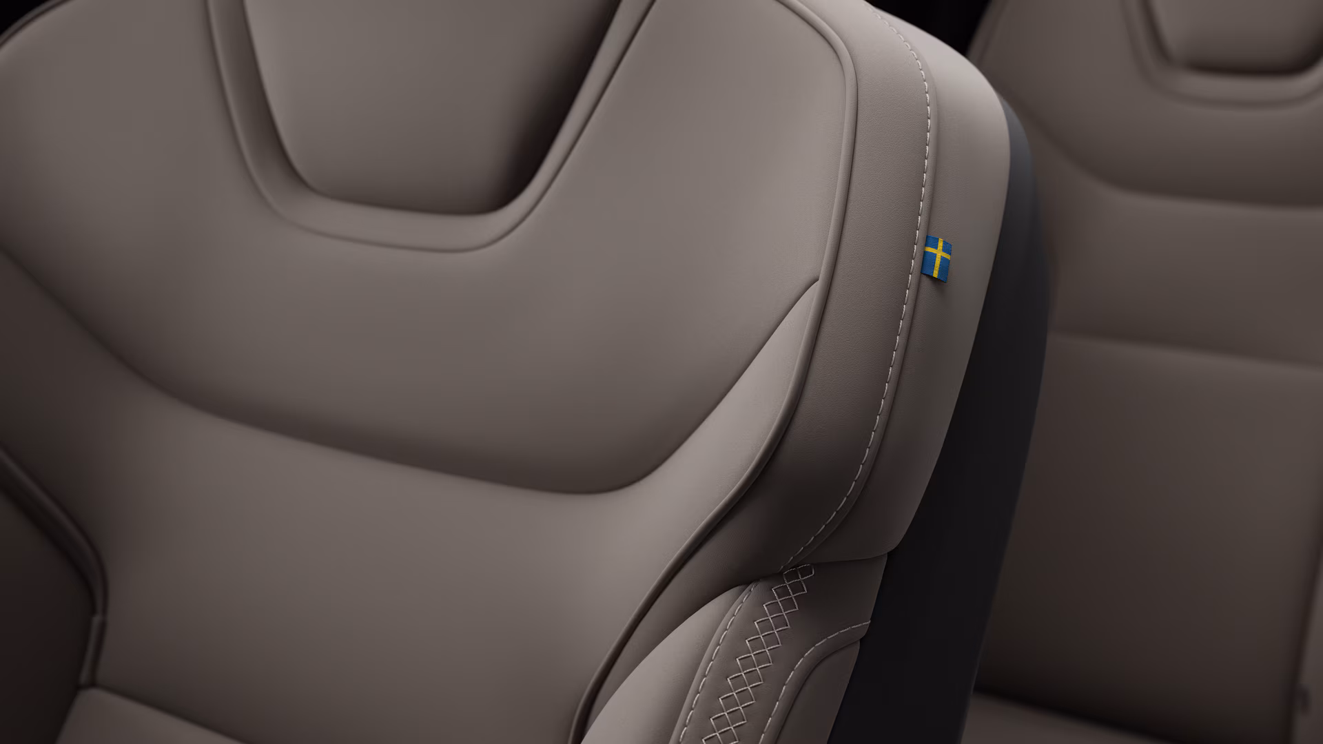Крупный план деталей салона автомобиля Volvo, на котором видны швы и маленькая бирка с шведским флагом.