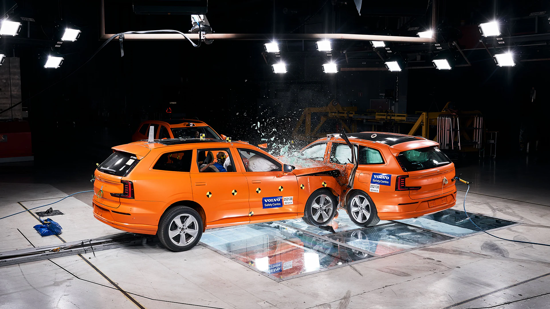 Два автомобиля Volvo проходят краш-тест на боковой удар в Центре безопасности Volvo, внутри видны манекены краш-тестов, а в месте удара разбивается стекло.