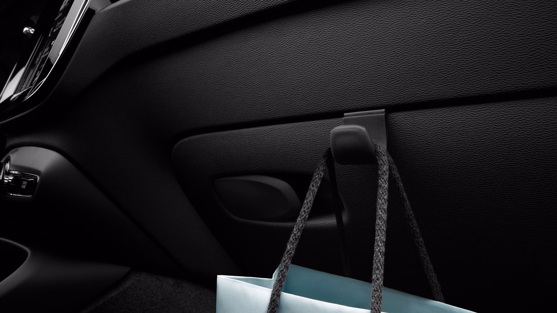 Крупный план салона Volvo: крючок на приборной панели, с которого свисает сумка с покупками.