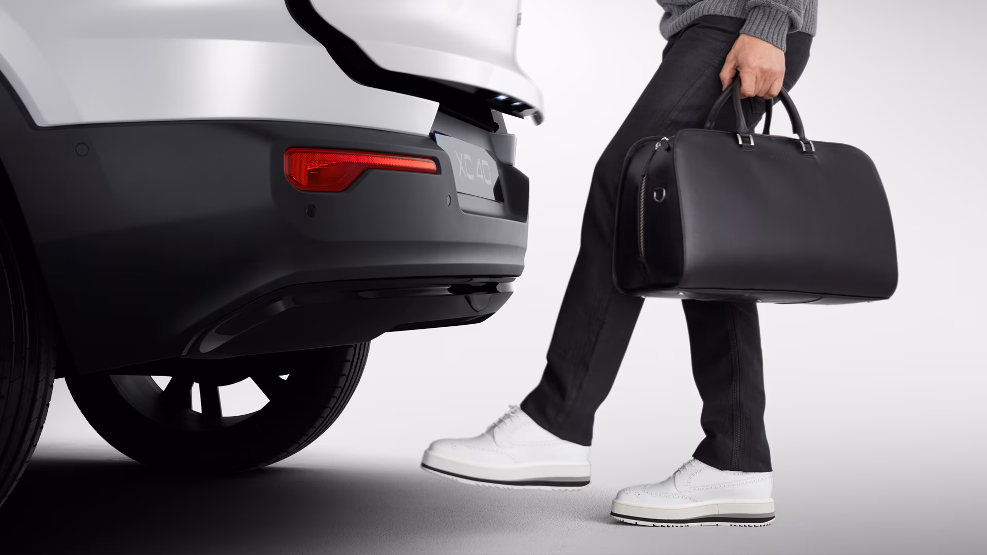 Человек с черной сумкой открывает заднюю часть Volvo XC40, двигая ногой рядом с бампером.
