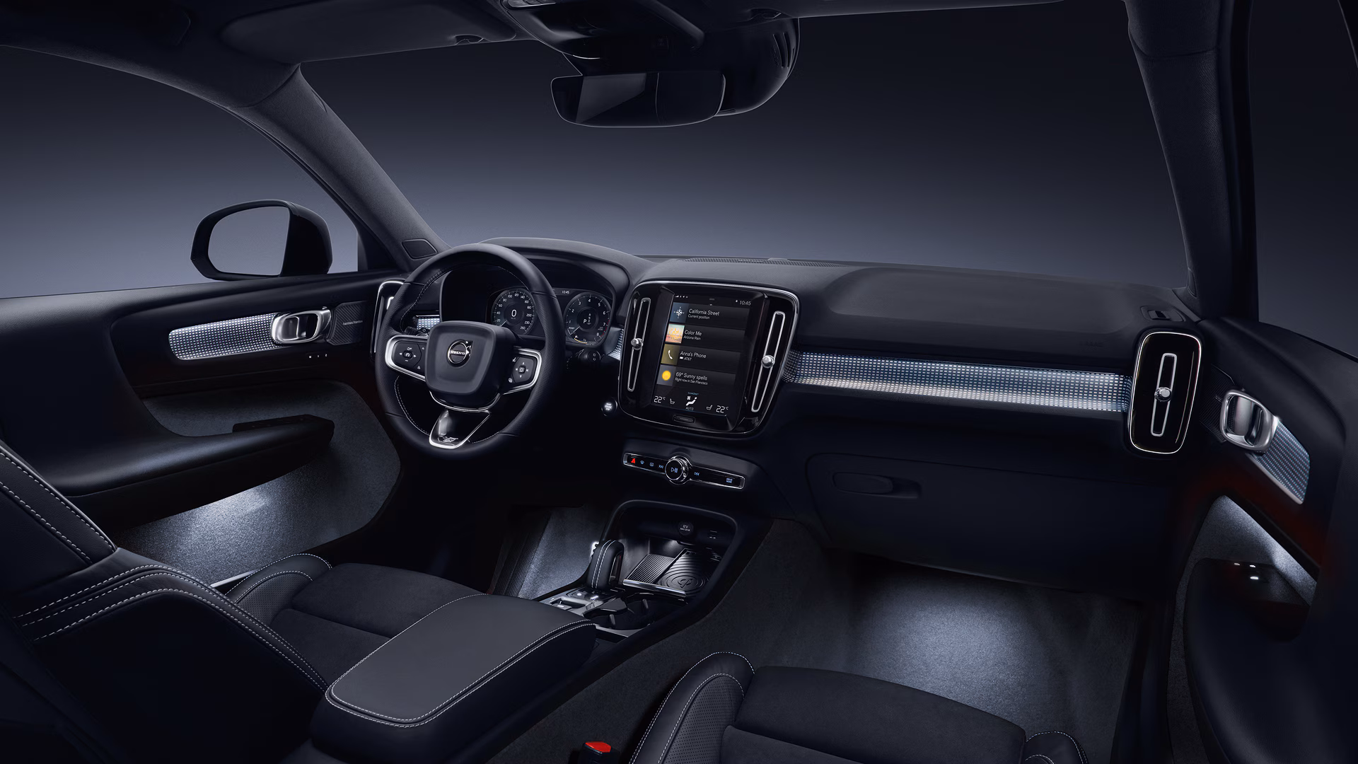 Вид салона автомобиля Volvo: сиденье водителя, руль с логотипом Volvo и центральный сенсорный дисплей на приборной панели.
