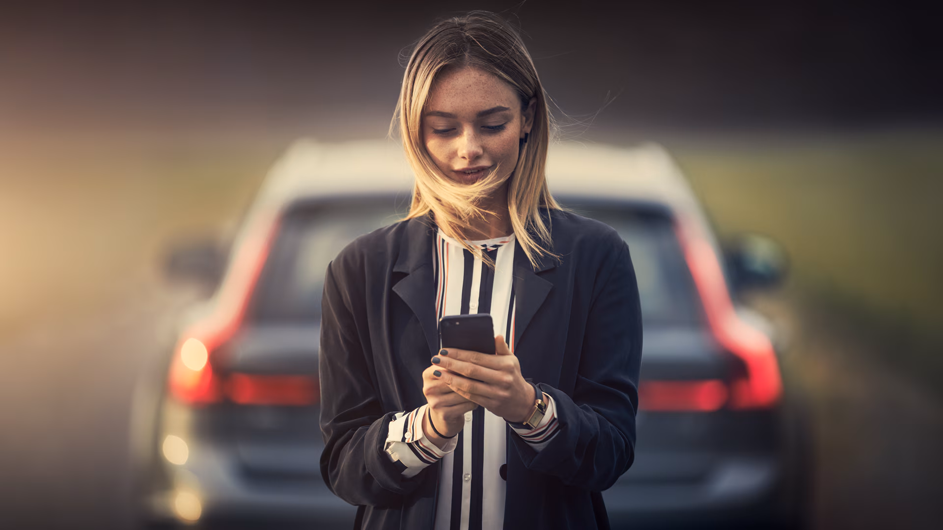 Человек стоит перед автомобилем Volvo на дороге со смартфоном в руке.