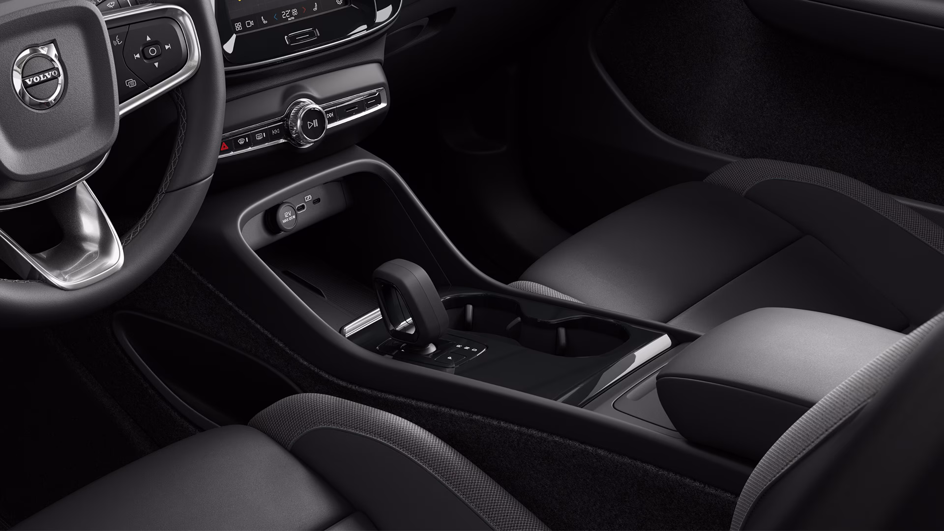 Вид изнутри автомобиля Volvo с рулевым колесом, центральной консолью и селектором передач с современными органами управления и отделкой.