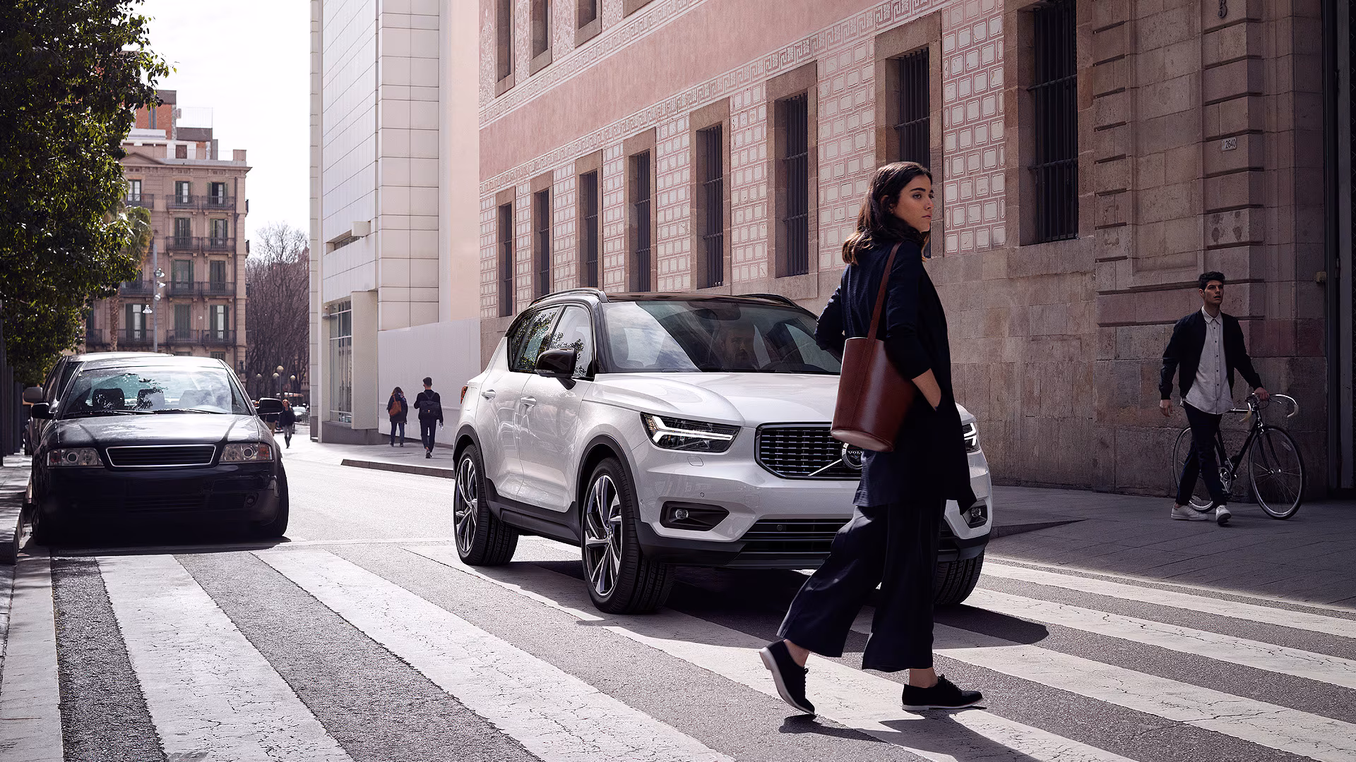 Белый Volvo XC40 останавливается на пешеходном переходе в городской среде, когда перед ним переходит дорогу пешеход.