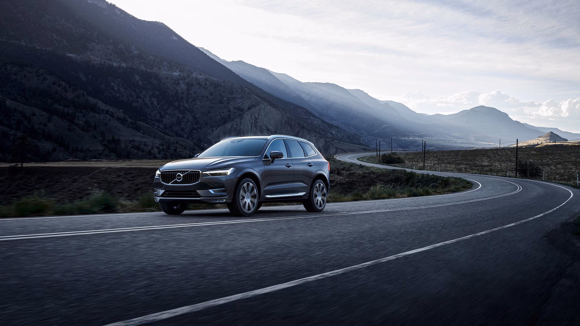 Внедорожник Volvo едет по извилистой горной дороге на фоне живописных холмов.