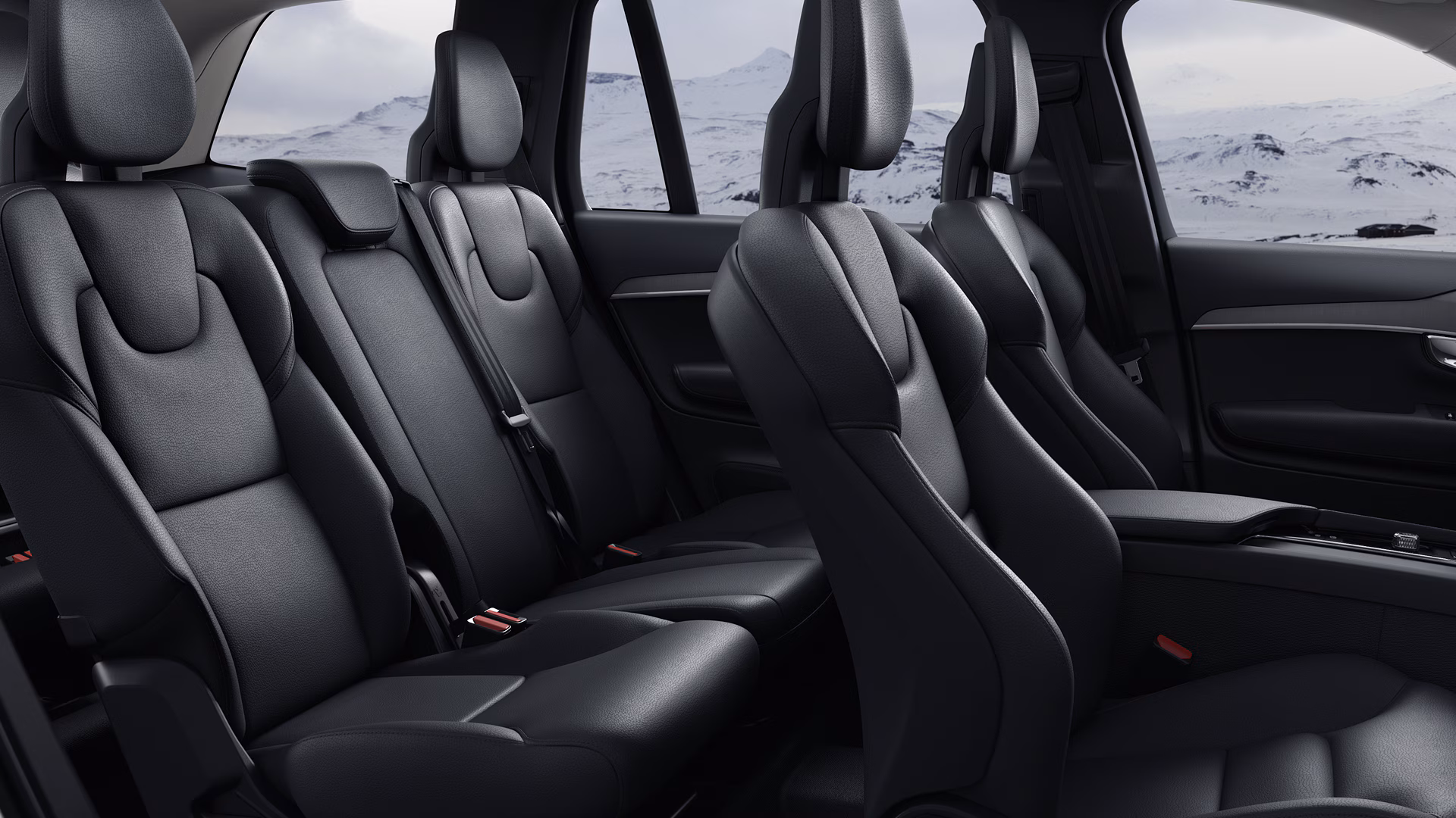 Вид изнутри автомобиля Volvo с двумя рядами черных сидений премиум-класса с достаточным пространством для ног и живописным заснеженным пейзажем, видимым из окон.