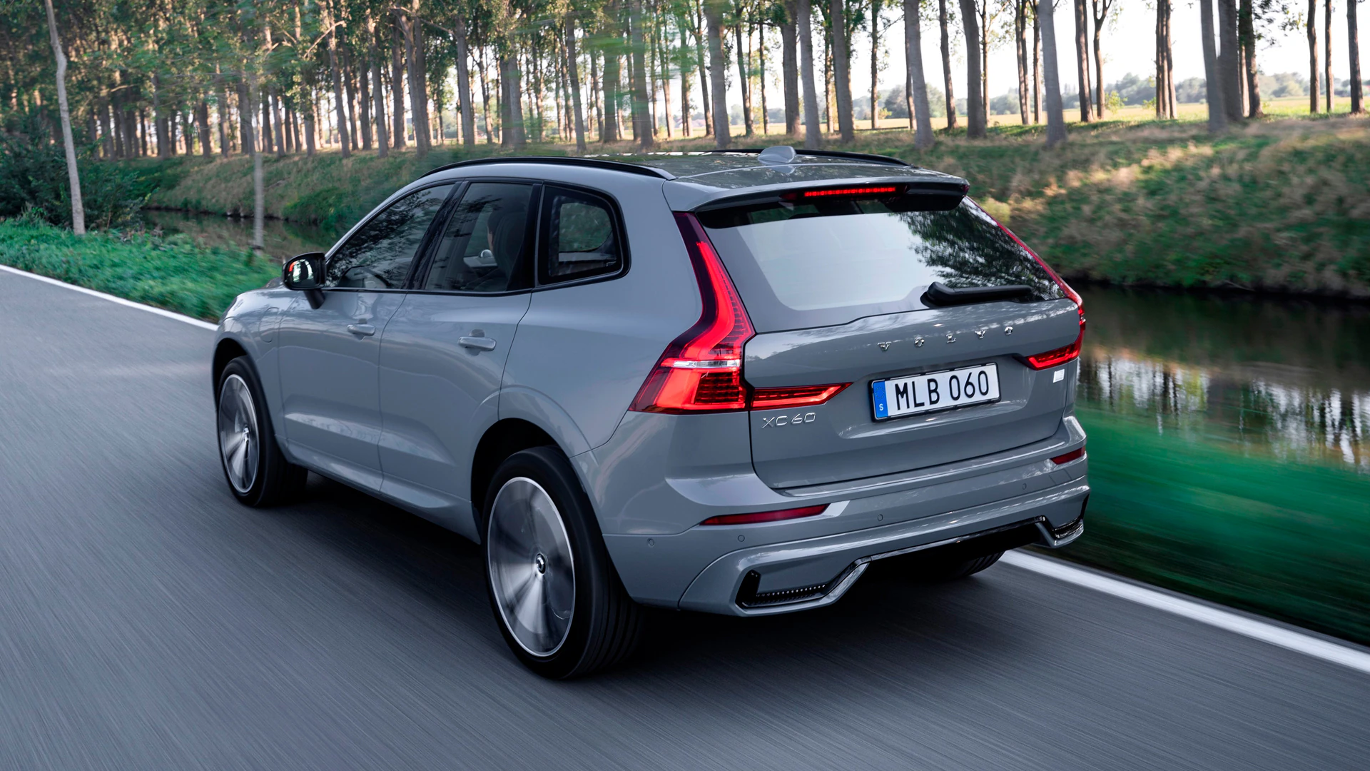 Вид сзади на Volvo XC60, едущий по живописной дороге, обсаженной деревьями.