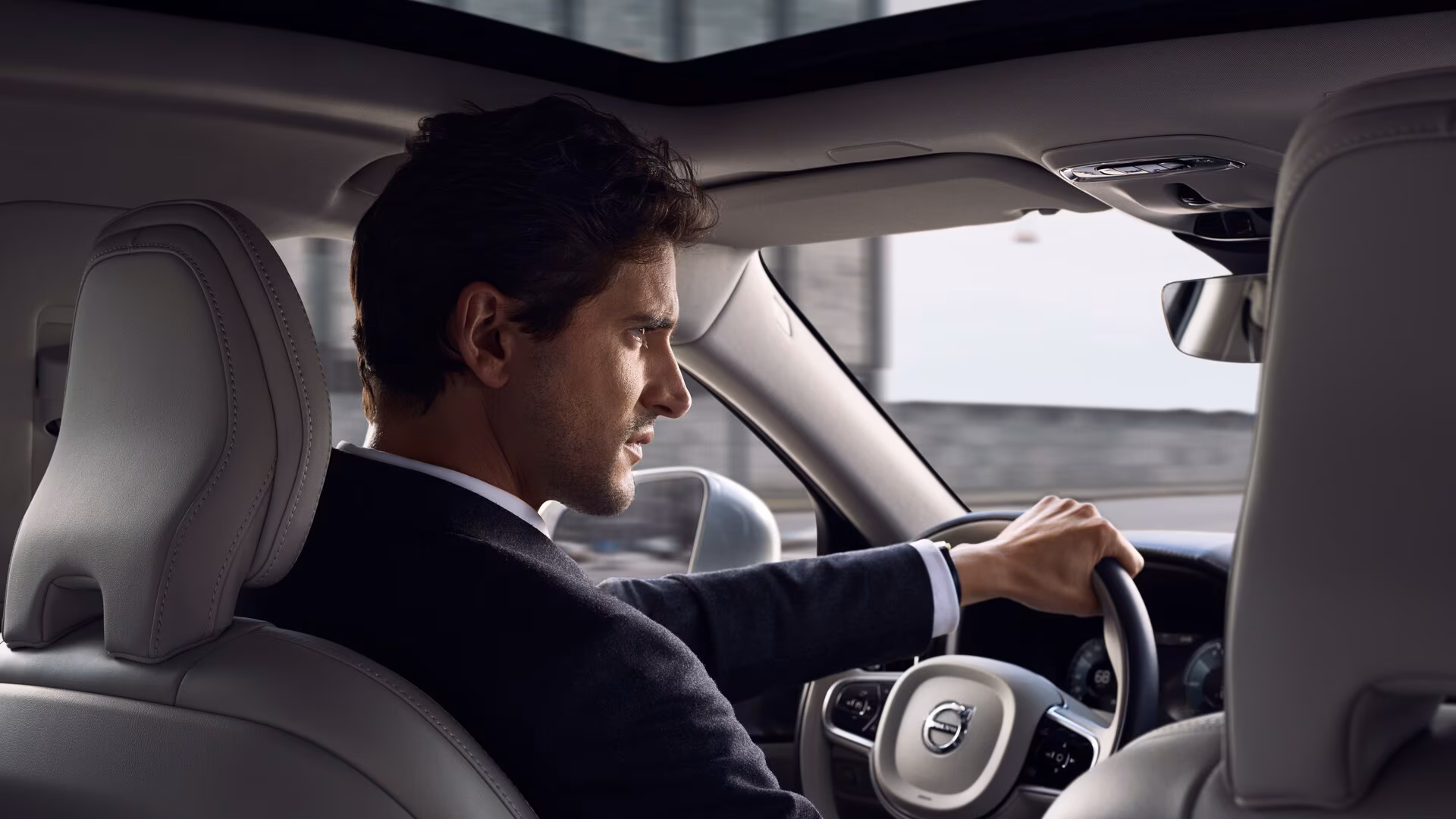 Вид с заднего сиденья, водитель держит руль автомобиля Volvo, подчеркивая дизайн интерьера и приборную панель.