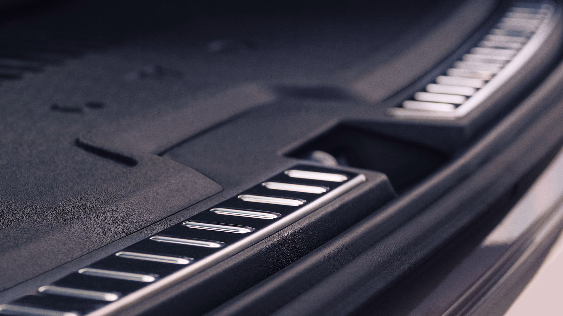 Крупный план багажного отделения автомобиля Volvo с защитной металлической накладкой порога на кромке багажника.