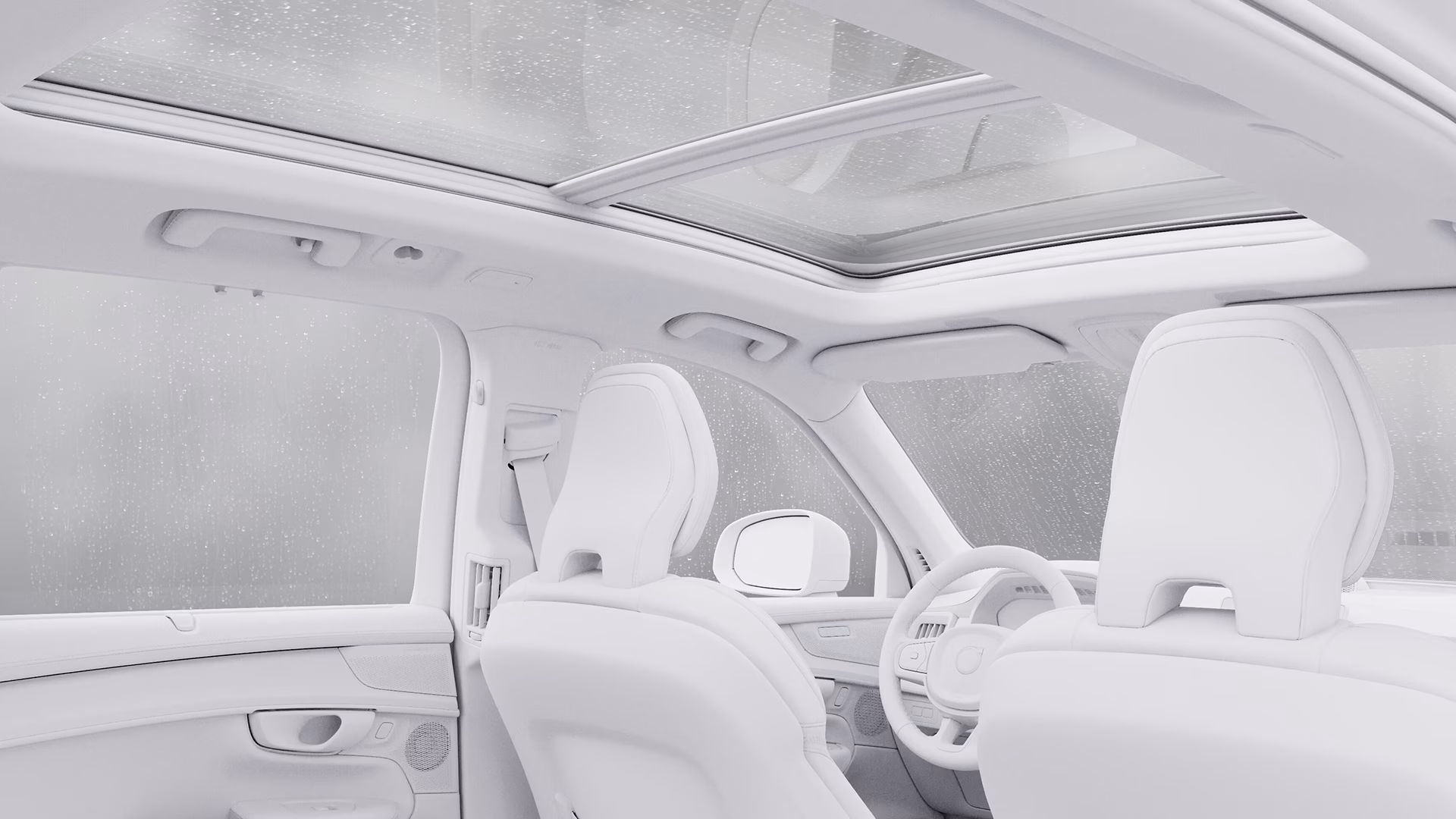 Вид изнутри автомобиля Volvo с белыми сиденьями и большой панорамной стеклянной крышей, на окнах которого виден дождь.